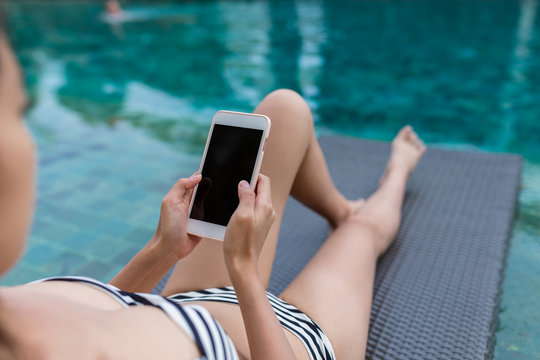 Woman using mobile phone at poolside on holiday