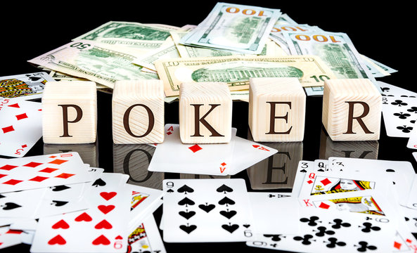 Word "Poker" written on wooden cubes with money and playing cards on black reflective background.