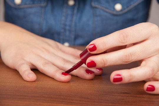 Frau lackiert sich Fingernägel mit rotem Nagellack