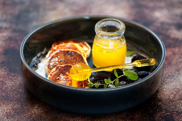 Cottage cheese pancakes with berries and honey on brown background