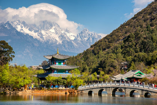 Fototapeta Amazing view of the Jade Dragon Snow Mountain and the Black Dragon Pool, Lijiang, Yunnan province, China. The Suocui Bridge over pond and the Moon Embracing Pavilion in the Jade Spring Park.