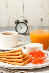 Breakfast. Thin pancakes with red caviar in white bowl on the table. Crepes. Coffee and juice. Selective focus