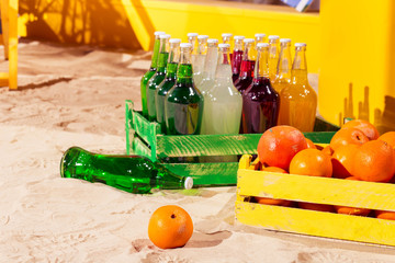 Orange wood box and lemonade bottles in summer sunny time on beach of ocean with palm leaves useful for background