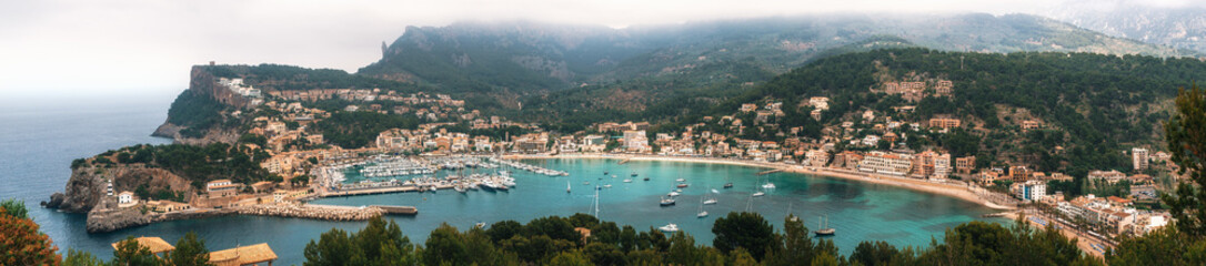 Fototapeta na wymiar Panoramic view of Port de Soller with harbour, yachts, tourist boats, colorful architecture and beach on a cloudy day. Landmark of Mallorca, Spain