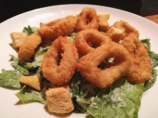 Stylist food, deep fried calamari on white plate serve with Caesar Salad on the wooden table with blur restaurant table background, closed up