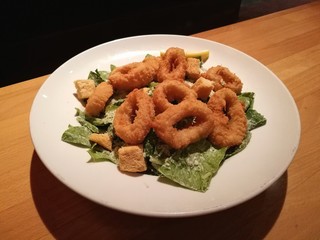 Stylist food, deep fried calamari on white plate serve with Caesar Salad on the wooden table with blur restaurant table background, top view
