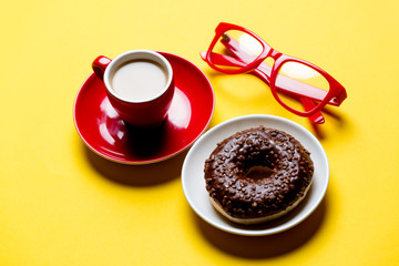 cool glasses, tasty glazed donut and cup of coffee on plates on the wonderful yellow background