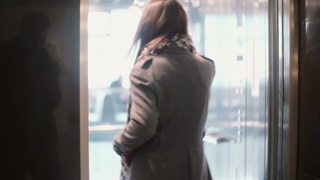 Young woman talking on the smartphone, coming into the elevator and smiling. The lift door is closed.