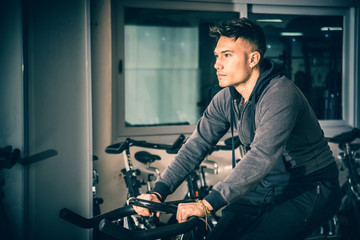 Fototapeta na wymiar Attractive young man exercise in gym: spinning, exercising on stationary bike
