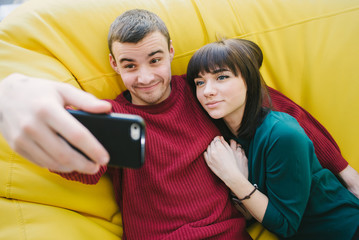 Fototapeta premium A young couple in love hipster fun doing selfie on your smartphone. Portrait of young people in the room.