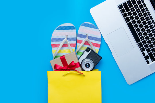 colorful sandals, camera and gift in shopping bag and cool laptop on the wonderful blue background