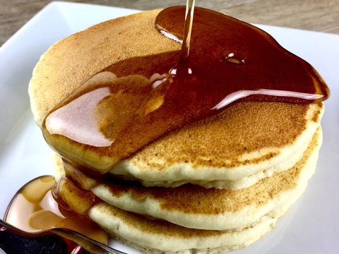 Stack of pancakes with maple syrup on a white plate