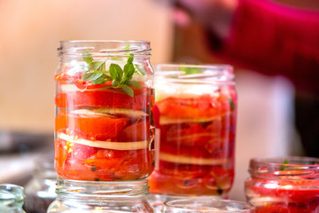 Plakat Canning fresh tomatoes with onions for winter in jelly marinade. A shot of basil leaves on top of a red ripe tomato slices and onion rings being put in jar.