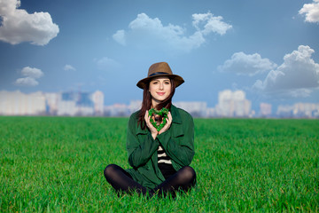 Naklejka na ściany i meble beautiful young woman sitting on the grass with heart shaped toy on the wonderful green field
