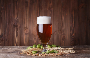 Glass of dark beer and its ingredients on table against blurred wooden background