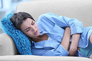 Young woman suffering from abdominal pain while lying on sofa at home. Gynecology concept
