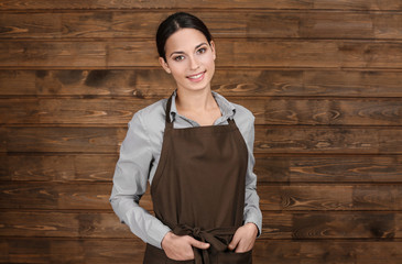 Young woman in apron standing on wooden background