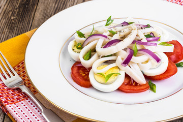 Salad with squid, egg and tomato on white plate on background of