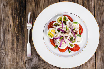 Salad with squid, egg and tomato on white plate on background of