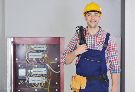 Young electrician with tools standing near open distribution board