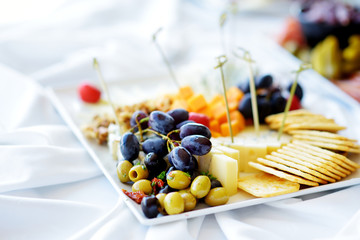 Different kinds of wine snacks: cheeses, crackers, fruits and olives on white table
