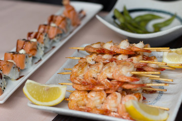 Sushi on a table. Shrimps, tiger rolls and edamame on white plates