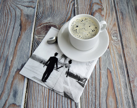 Чашка с кофе и салфетка с символом Парижа   лежат на деревянном столе