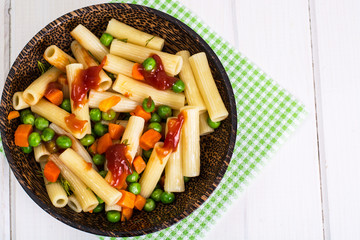 Pasta with carrots and green peas in wooden bowl