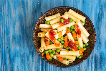Pasta with carrots and green peas in wooden bowl