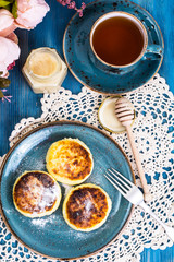Cottage cheese fritters, honey and tea in a vintage cup on a blu
