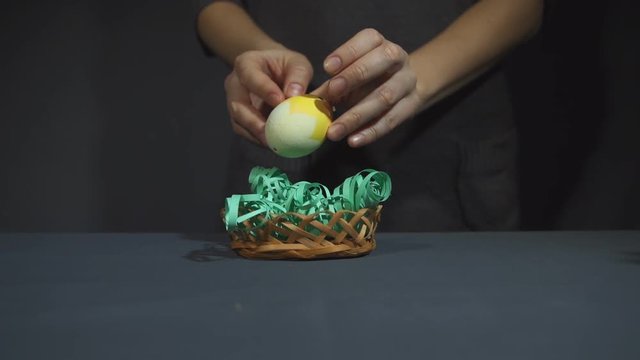Female hands put on the grey table small bamboo basket with paper grass in it, inserted with yellow chickens of the eggshell, then on two sides of one install two chocolate easter bunny close up.