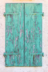 Old vintage retro wooden turquoise cracked paint window blinds, shutter  on white stone wall as architecture background
