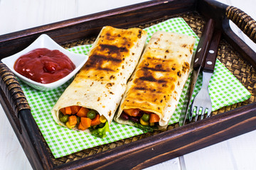 Burritos with vegetables on wooden tray