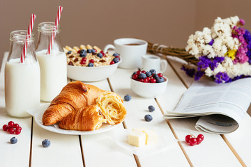 Tasty breakfast with croissant, oat flakes, berries and milk on the white wooden table