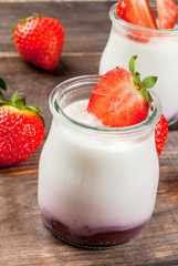 Fresh homemade yogurt with strawberries, decorated with strawberry slices and mint leaves. On a wooden table, with strawberries, copy space