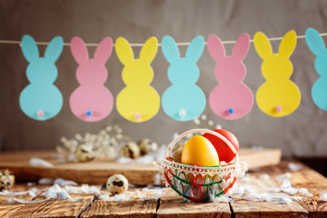 Easter composition of Easter colorful eggs in the basket and with bunny garland on wooden background.