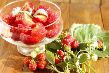 ripe strawberries in a transparent bowl and bunches with leaves