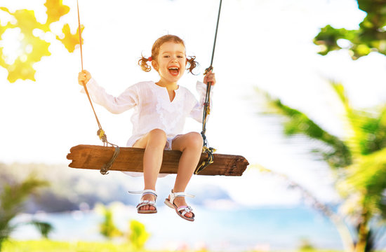 Happy child girl swinging on swing at beach  in summer
