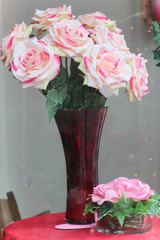 red vase full of cloth pink and white roses in window display