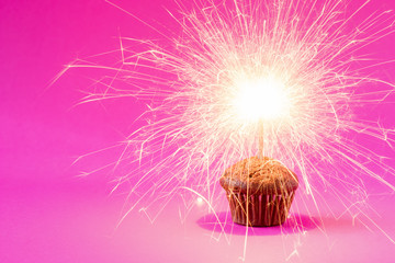 Cupcake with a sparkler over a pink background.