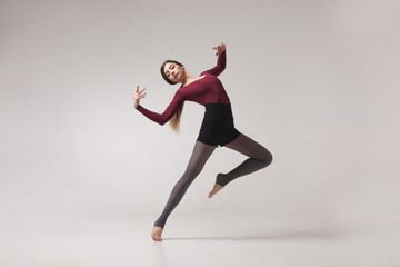 Fototapeta na wymiar young beautiful woman dancer with long brown hair wearing maroon swimsuit posing on a light grey studio background