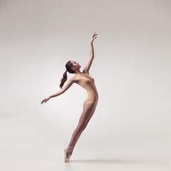 young beautiful ballet dancer in beige swimsuit posing on pointes on light grey studio background - 139484798