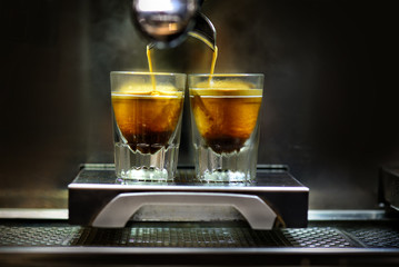 Professional coffee brewing. Coffee espresso. Close-up of espresso pouring from coffee machine to shotglasses.