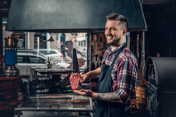 A man holds beef steak on a kitchen.
