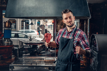 A man holds beef steak on a kitchen.