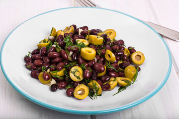 Salad with red beans and green olives in bowl on white boards