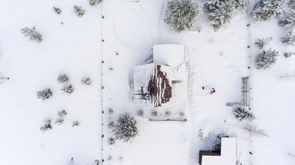 Top view at the timber house under snow in countryside. Courtyard with people playing in snowdrift.