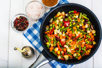 Vegetarian food: vegetables in frying pan on white wooden backgr