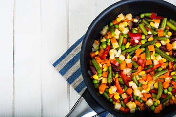 Vegetarian food: vegetables in frying pan on white wooden backgr