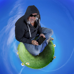 hipster man with hoodie sitting on a grass planet controls laptop